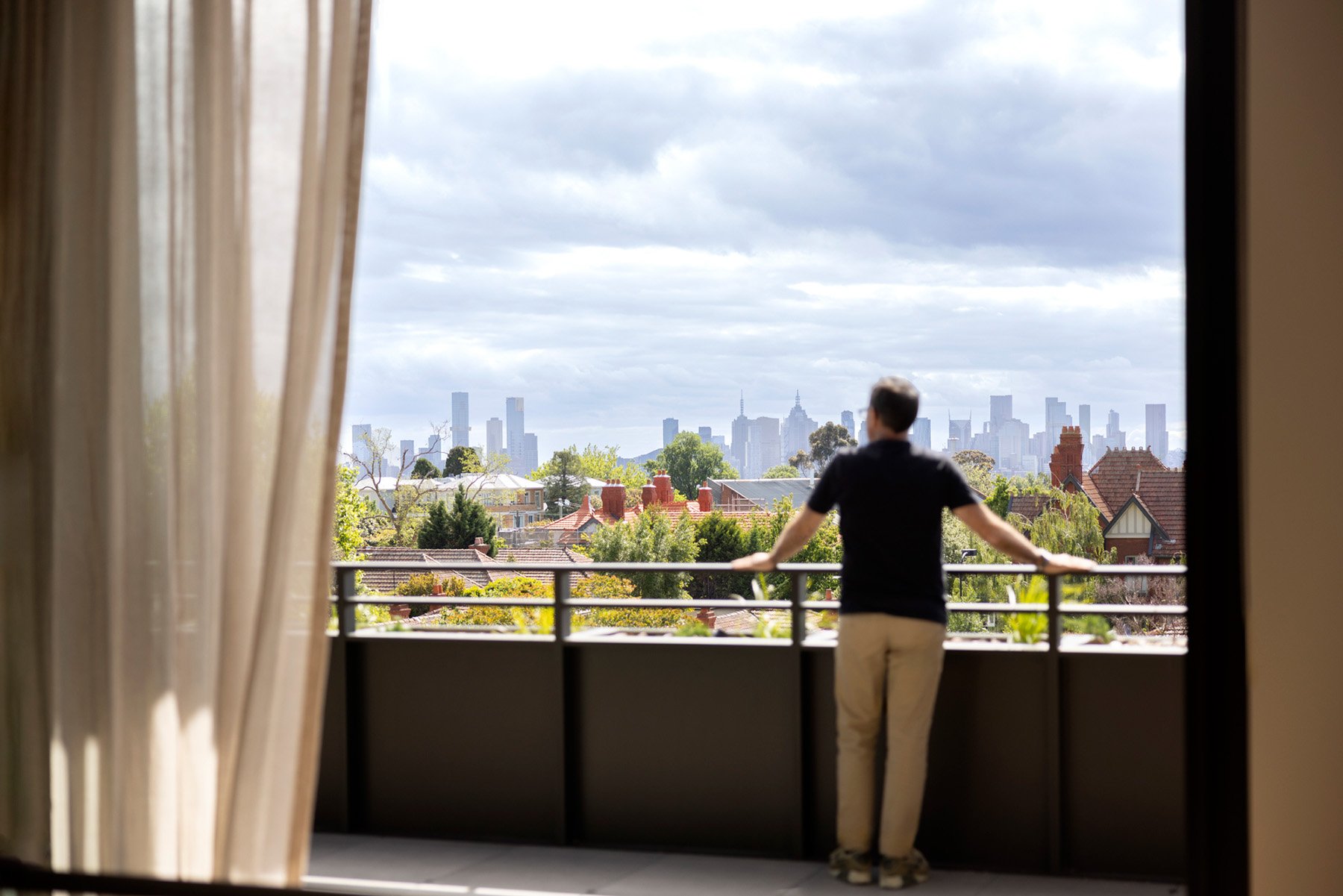 Resident stands at St. Clare balcony, view of Melbourne CBD in background